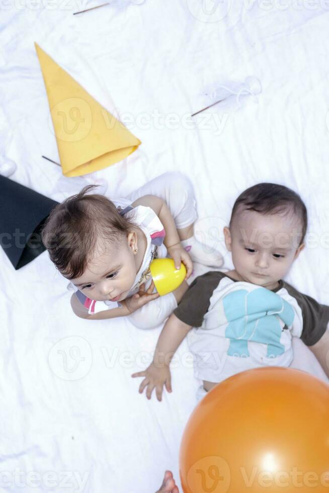 dos bebés jugando con globos y cumpleaños tapas. hermano y hermana jugando juntos foto