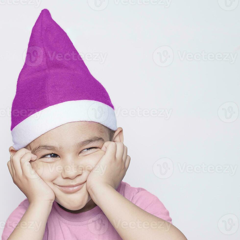 un pequeño niño haciendo gracioso irritado rostro. irritado Navidad chico en Papa Noel sombrero foto