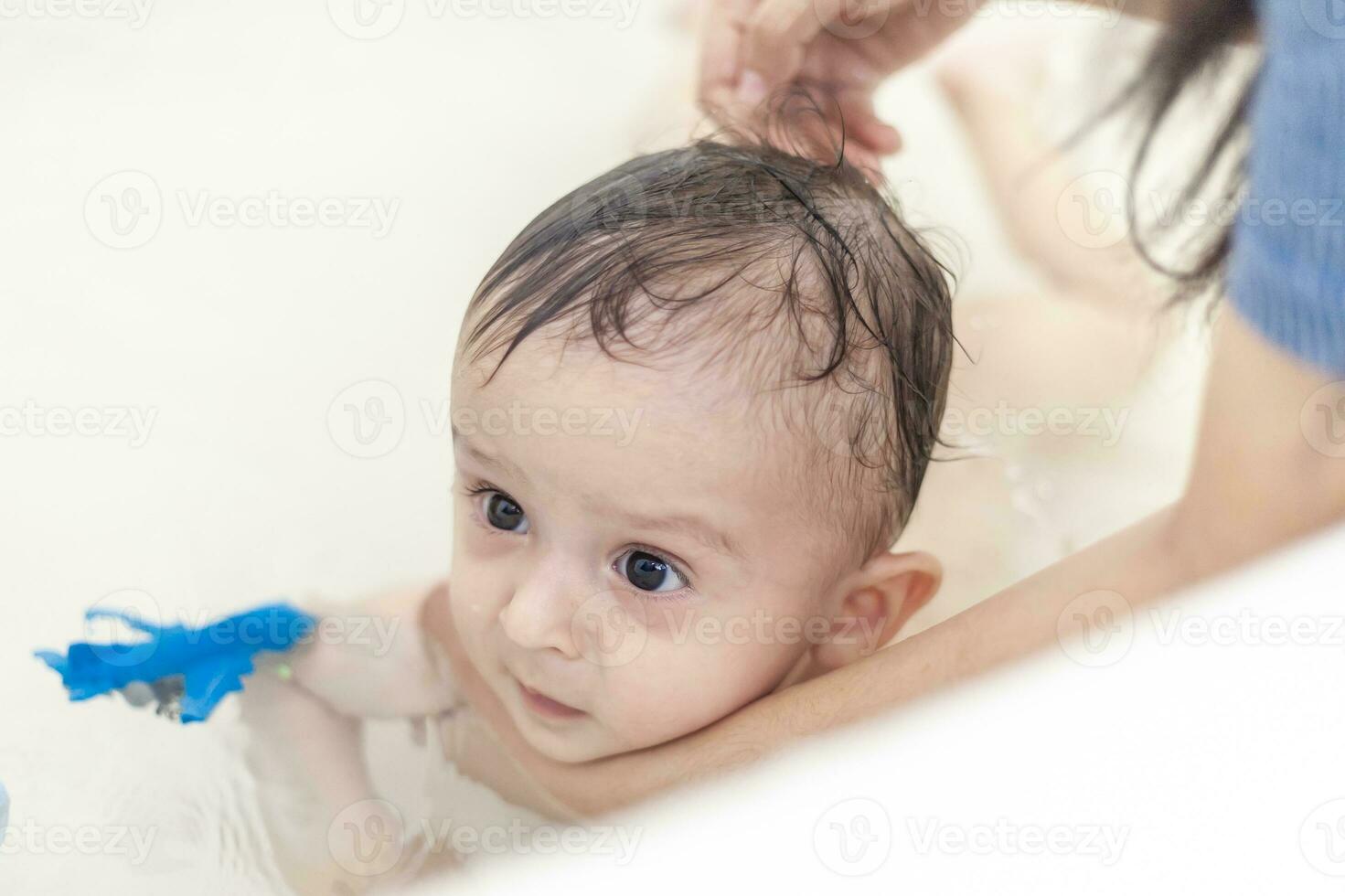 Young mom washing her baby boy's hair at bathroom. Mother bathing her baby photo