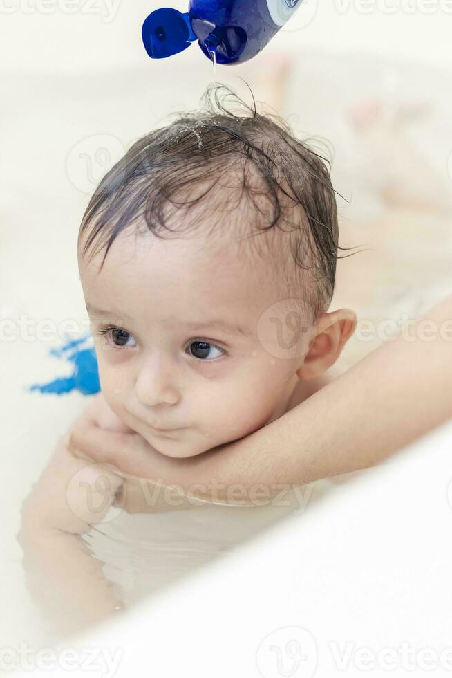 joven mamá Lavado su bebé Niños pelo a baño. madre baños su bebé foto