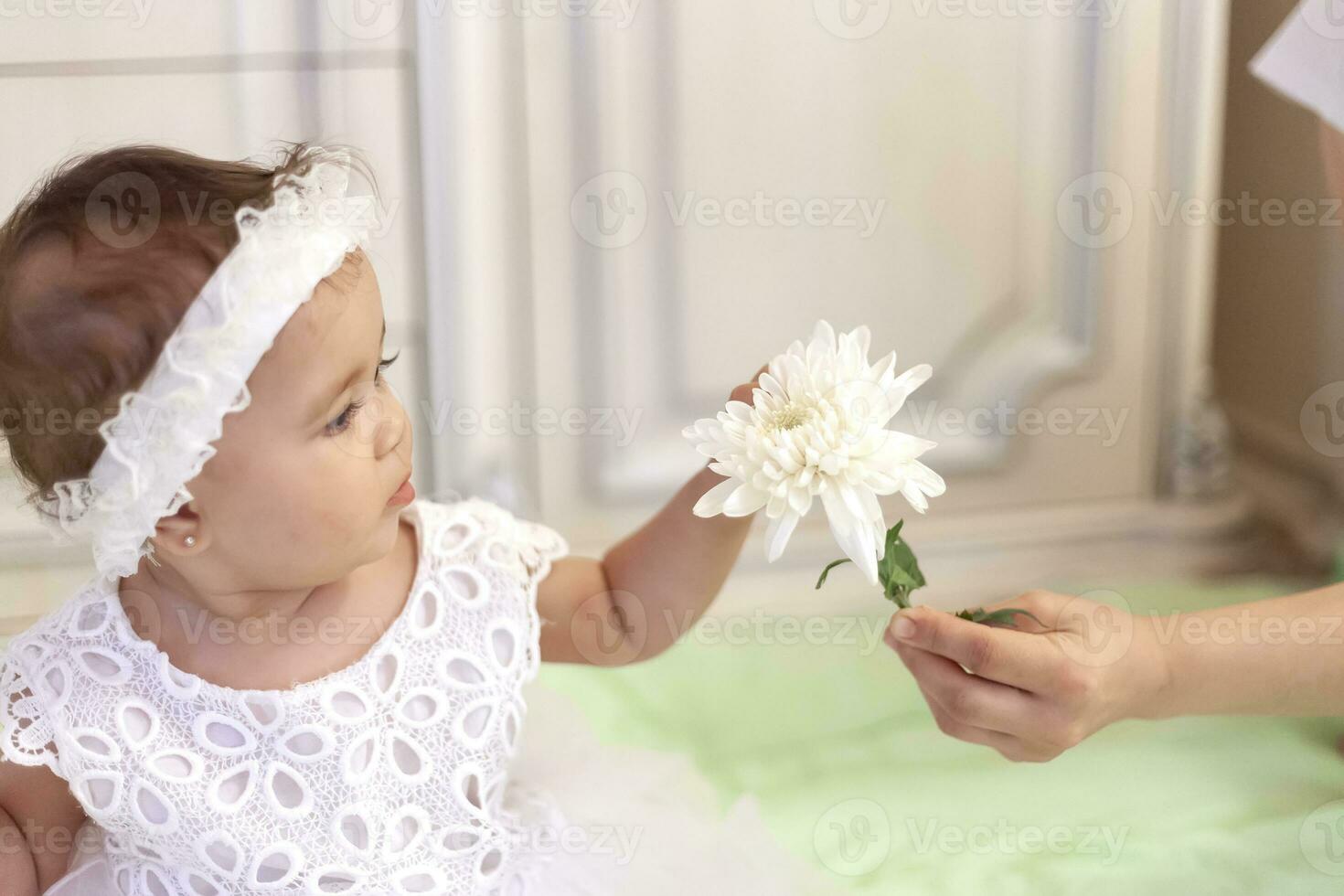 Baby girl in white dress taking a beautiful single white flower photo