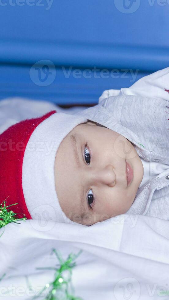 Little funny Santa boy playing with christmas or new year holiday festive garland. 1 year old baby boy in Santa Claus cap. photo