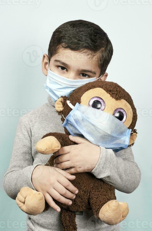 pequeño preescolar niño jugando con su juguete mono en médico cara máscara foto