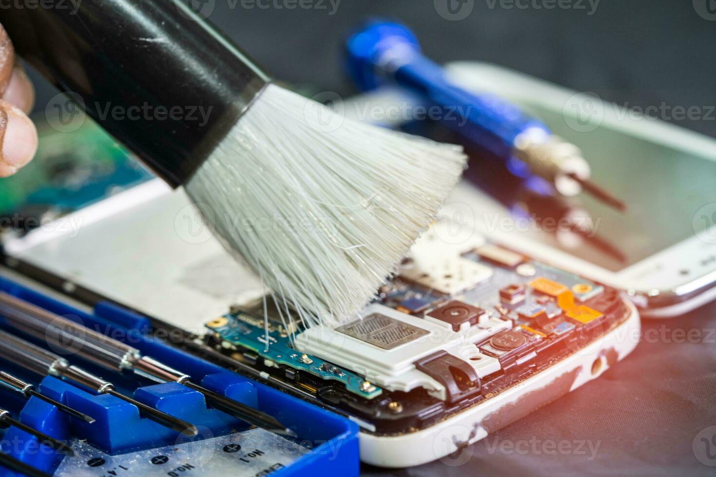 Asian technician repair and cleaning dirty micro circuit main board of smartphone electronic technology with brush, hardware, mobile phone, upgrade concept. photo