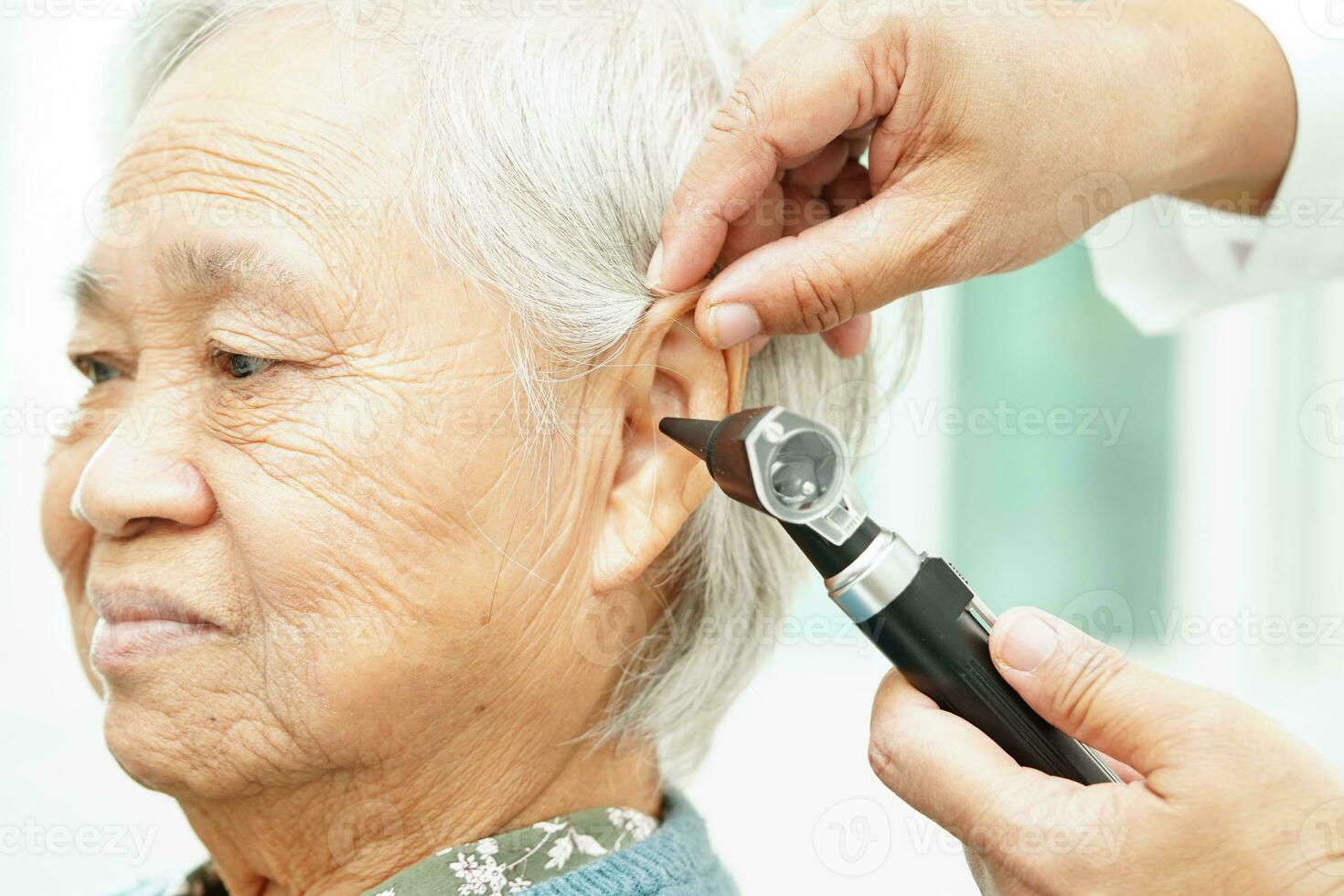 Otolaryngologist or ENT physician doctor examining senior patient ear with otoscope, hearing loss problem. photo
