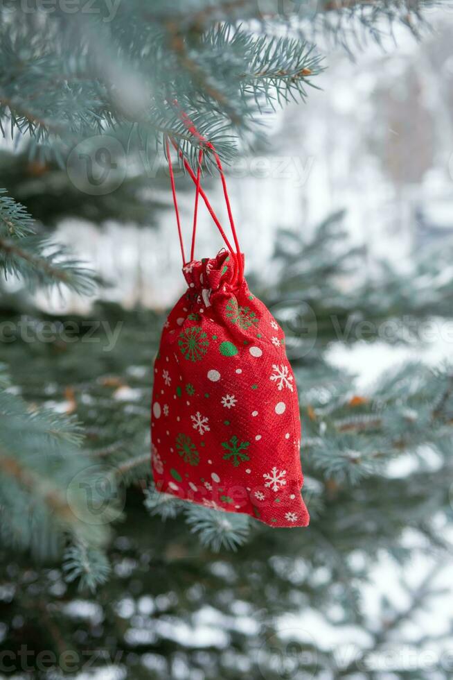 red Christmas gift is hanging on pine tree outdoors. photo