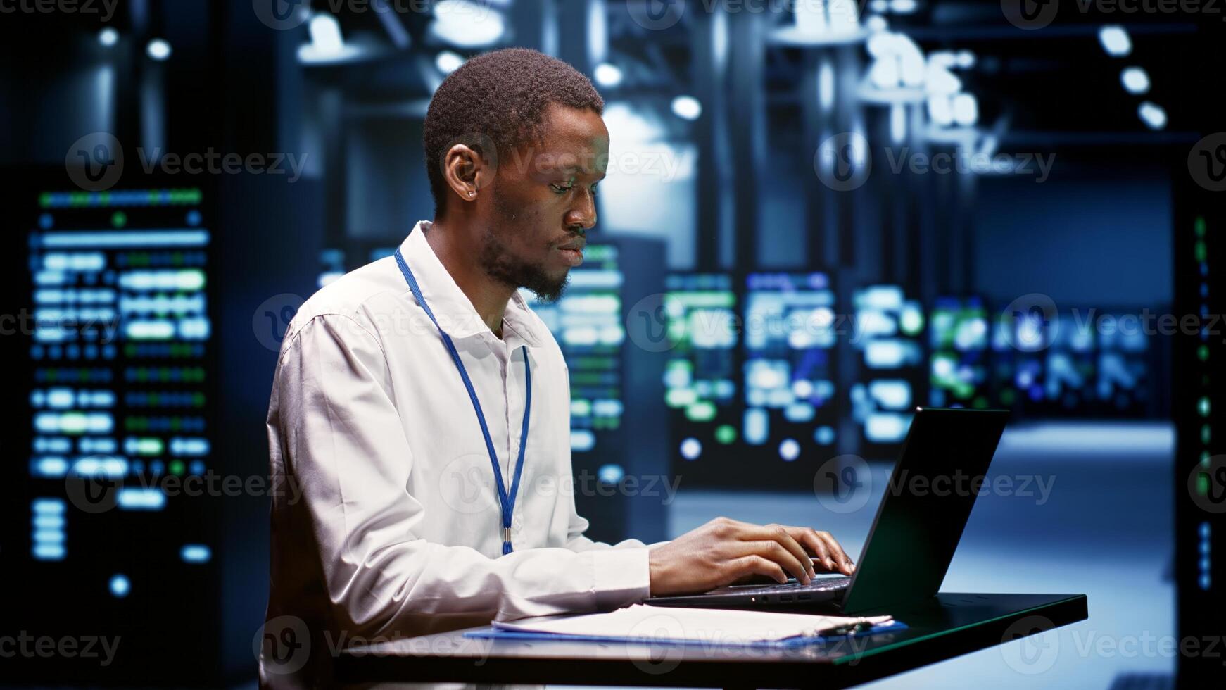 Computer scientist using laptop to debug servers cabinets helping companies manage databases, host websites and store files. Repairman reviewing high tech facility used for high performance computing photo