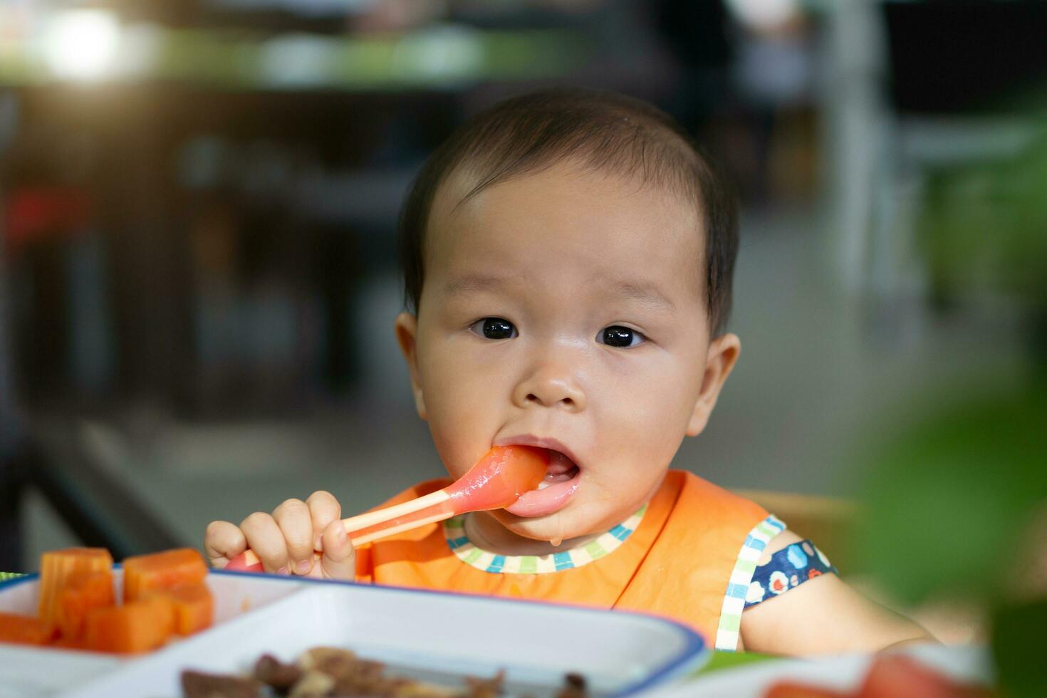 Asian baby girl in restaurant with a spoon eats food photo