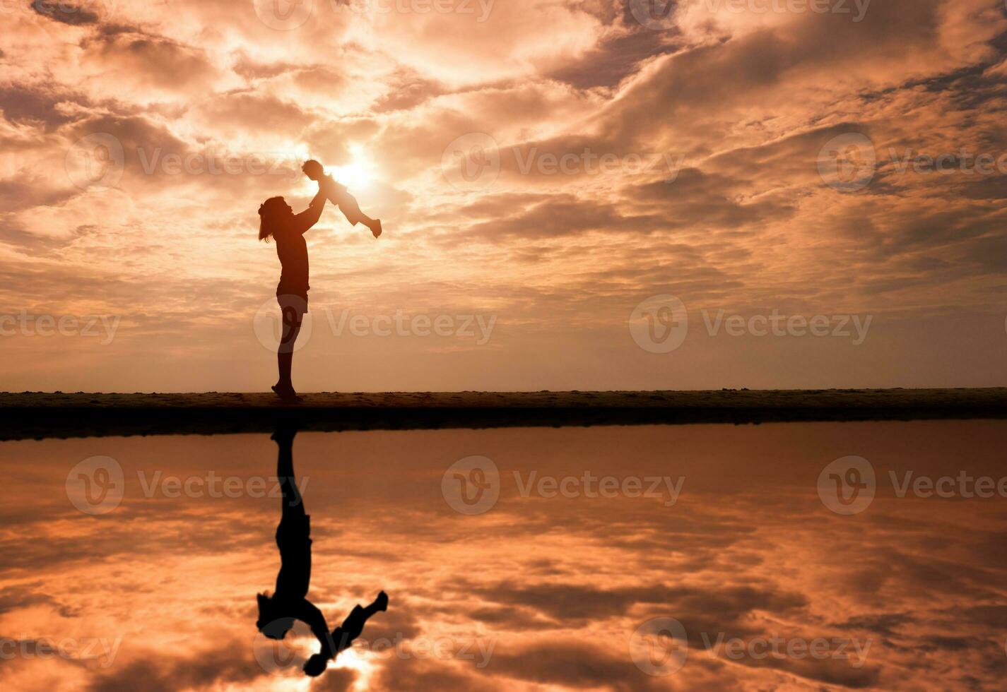 Reflection of Silhouette mother lift her toddler against the sunset photo