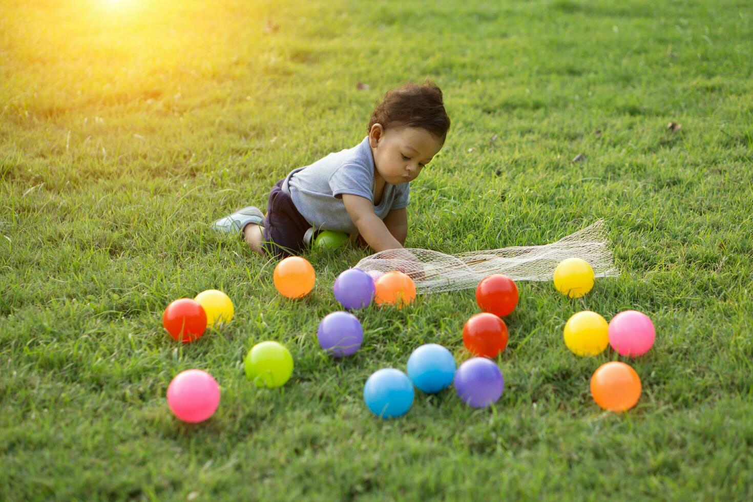 linda asiático bebé jugando vistoso pelota en verde césped foto