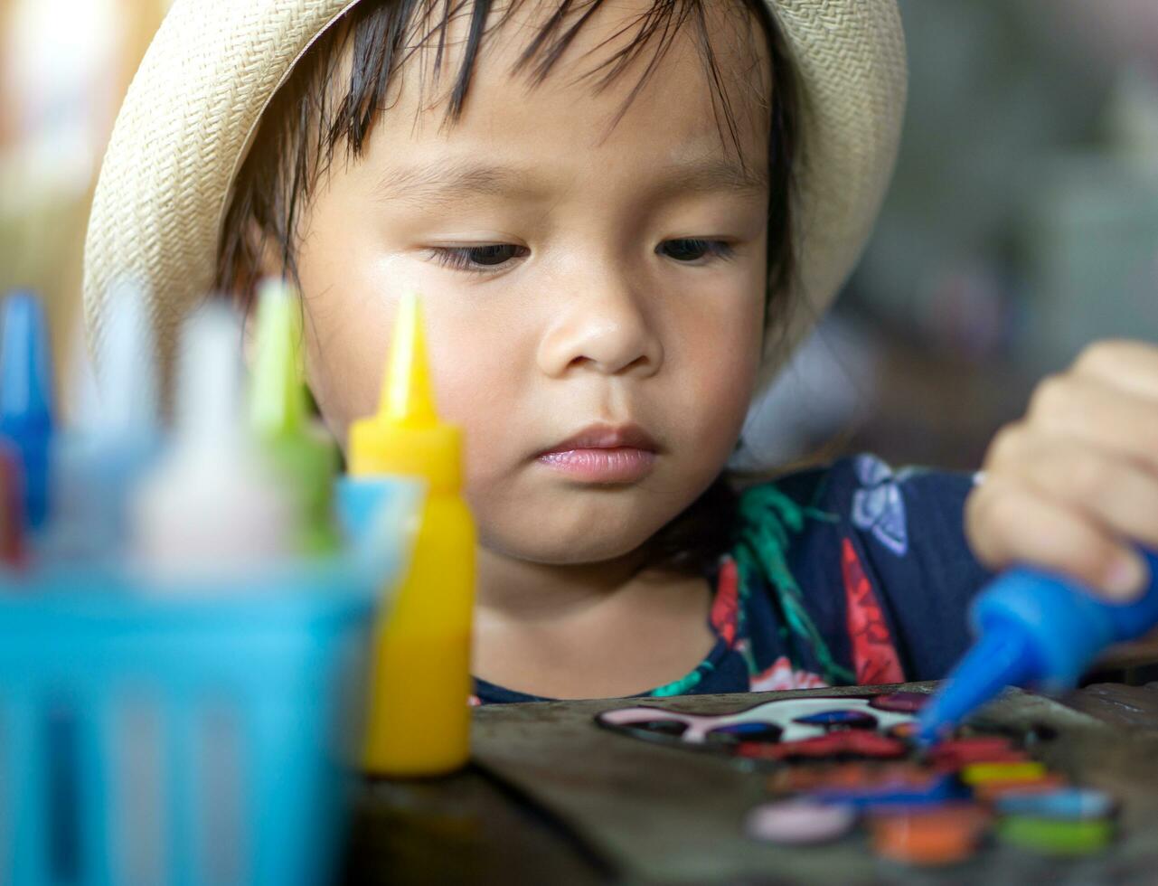 Asian kid is playing with plastic color paint on zinc sheet. photo