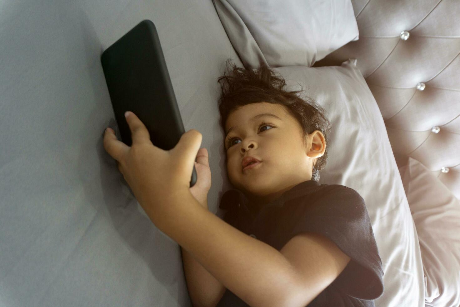 Asian thai kids lying on the bed and watching plays in the smartphone photo