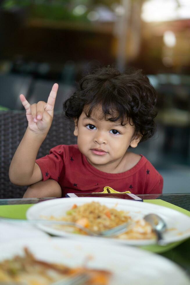 Rizado pelo asiático niño comiendo desayuno en un restaurante foto