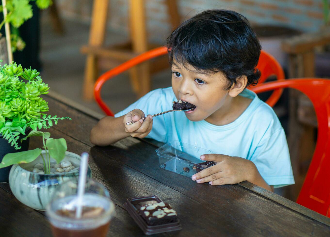 Asian boy is eating brownies on a wooden table photo