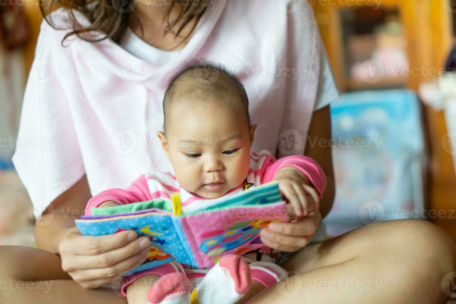 6-month-old Asian girl sat on the mother's lap and reading a children's story book. photo