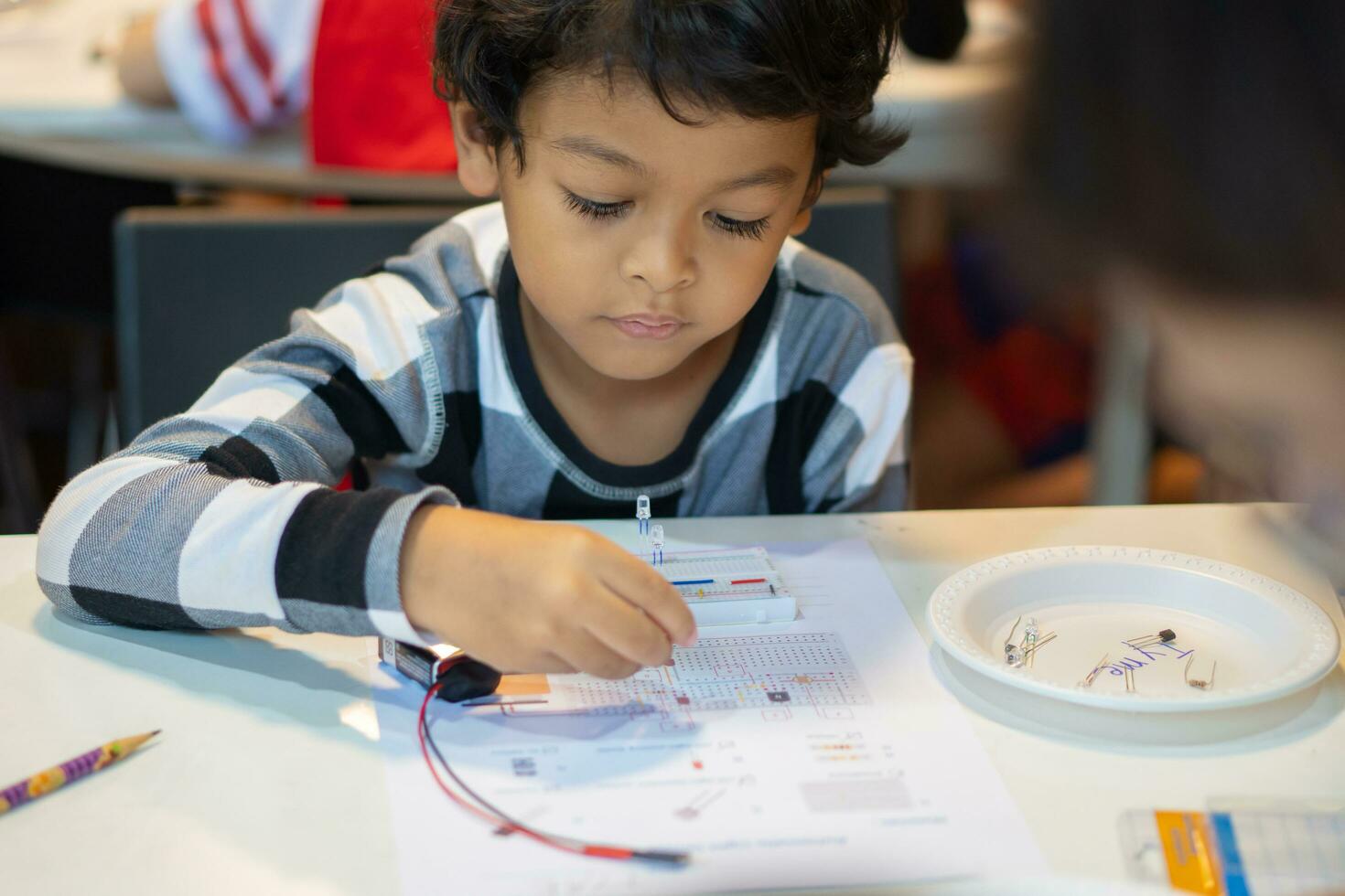 niño aprender a conectar eléctrico circuitos en el aula. foto