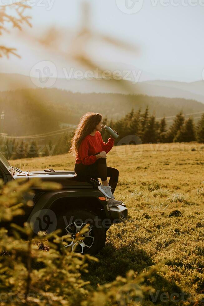 Young woman relaxing on a terrain vehicle hood at countryside photo