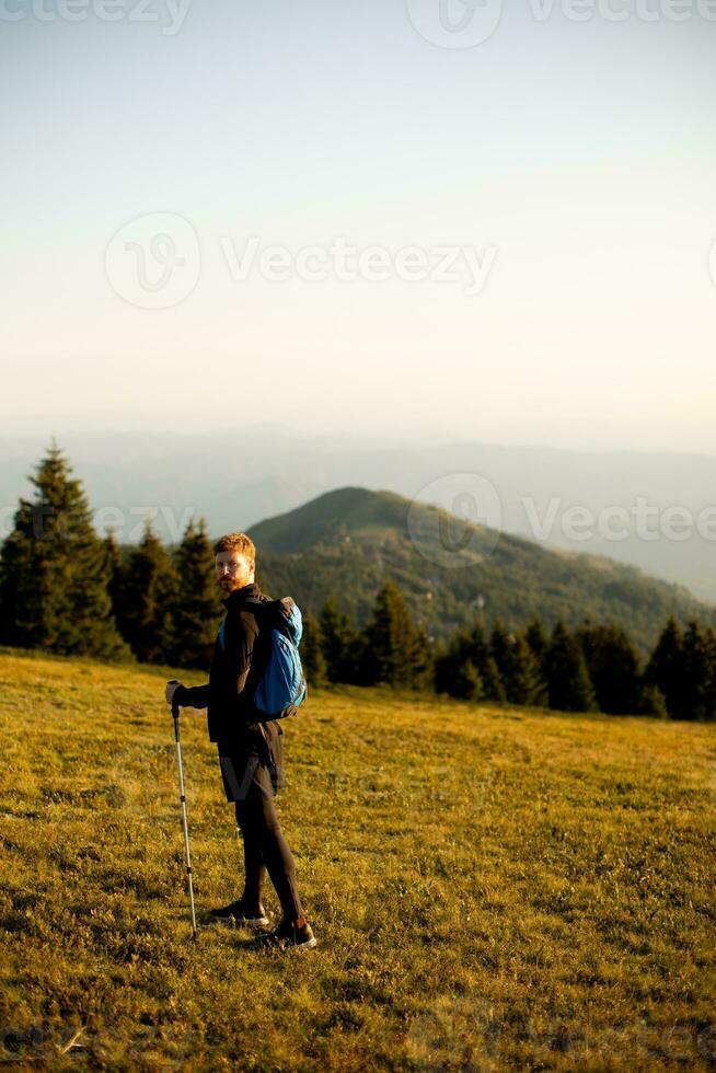 Young man walking with backpack over green hills photo
