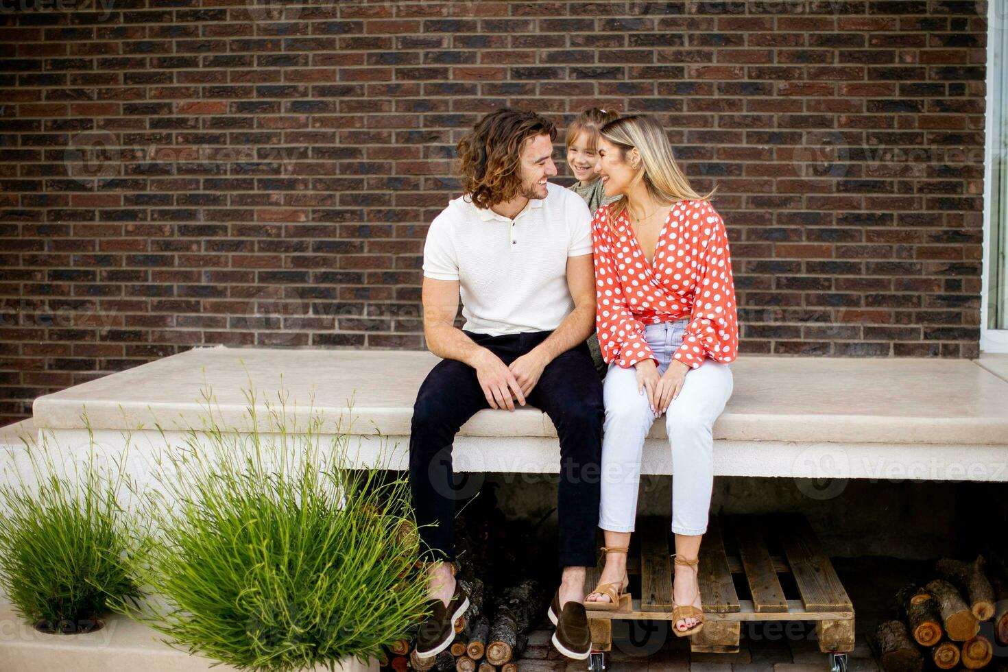 Family with a mother, father and daughter sitting outside on the steps of a front porch of a brick house photo