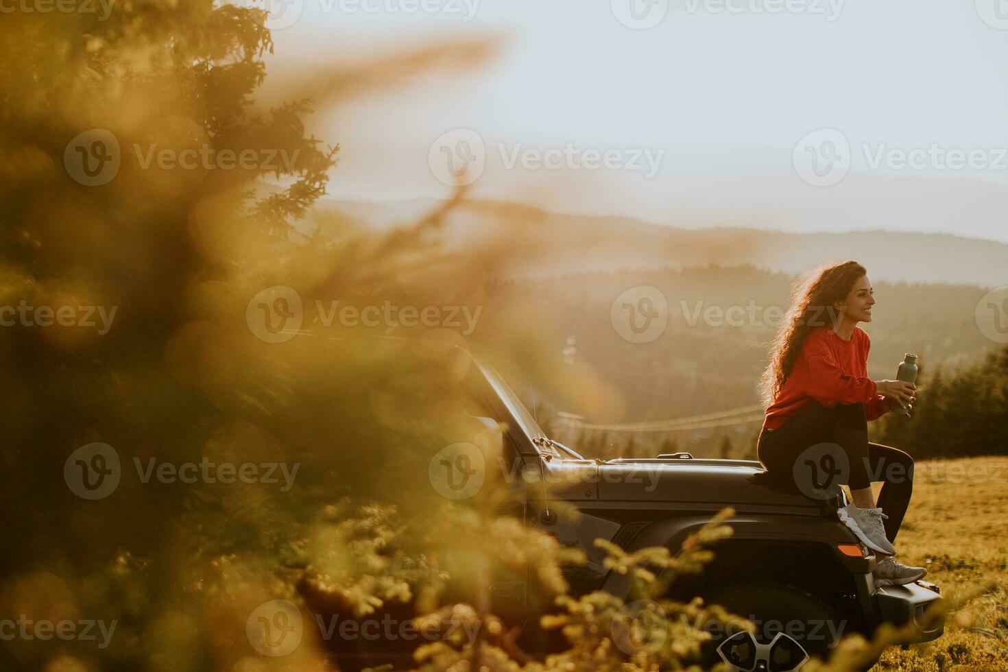 Young woman relaxing on a terrain vehicle hood at countryside photo