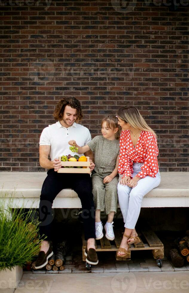 Family with a mother, father and daughter sitting outside on the steps of a front porch of a brick house photo