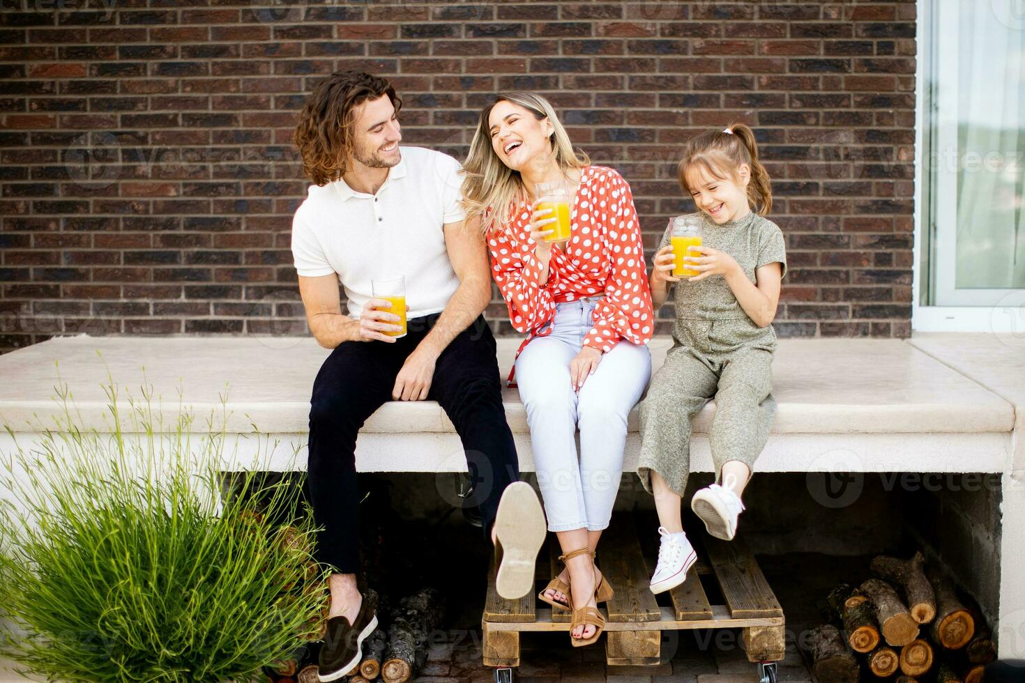 Family with a mother, father and daughter sitting outside on the steps of a front porch of a brick house photo