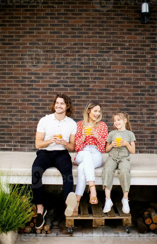 Family with a mother, father and daughter sitting outside on the steps of a front porch of a brick house photo