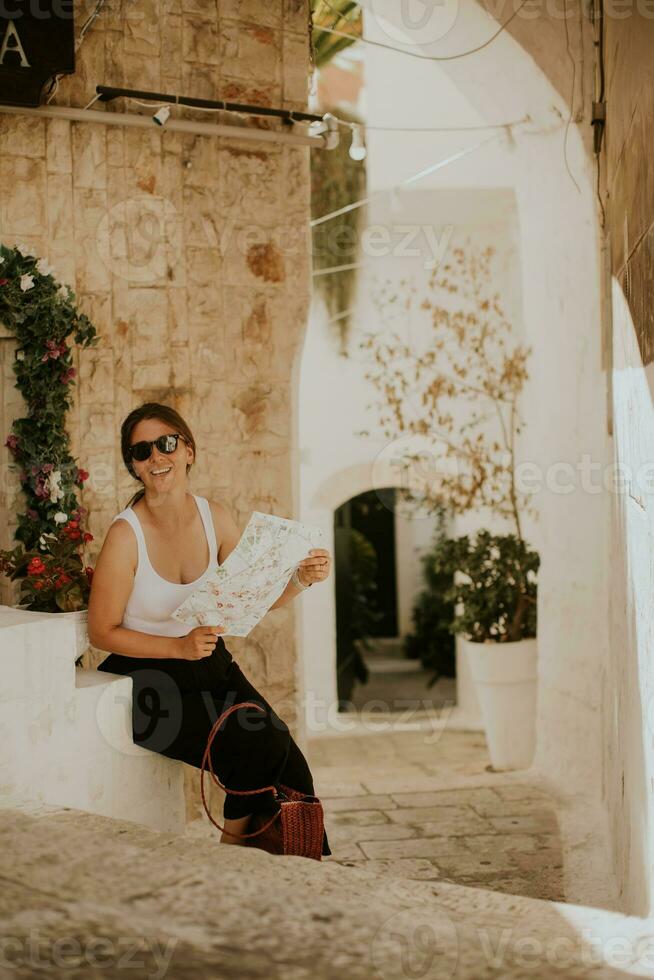 Female tourist with paper city map on narrow streets of Ostuni, Italy photo