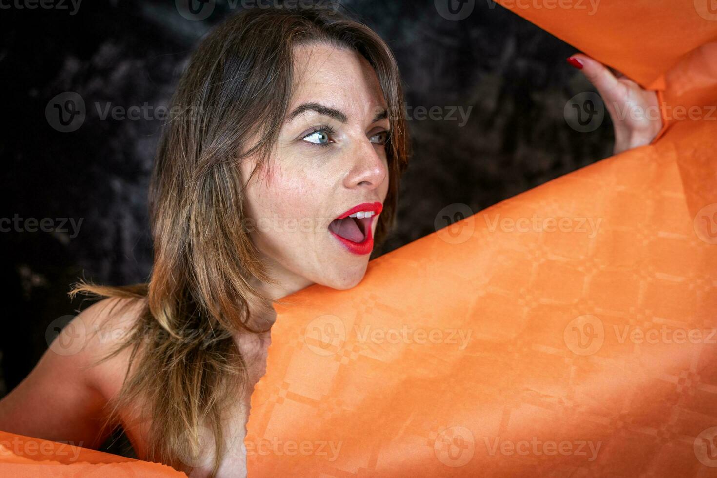 portrait of attractive young woman is coming out of a hole in a sheet of paper photo