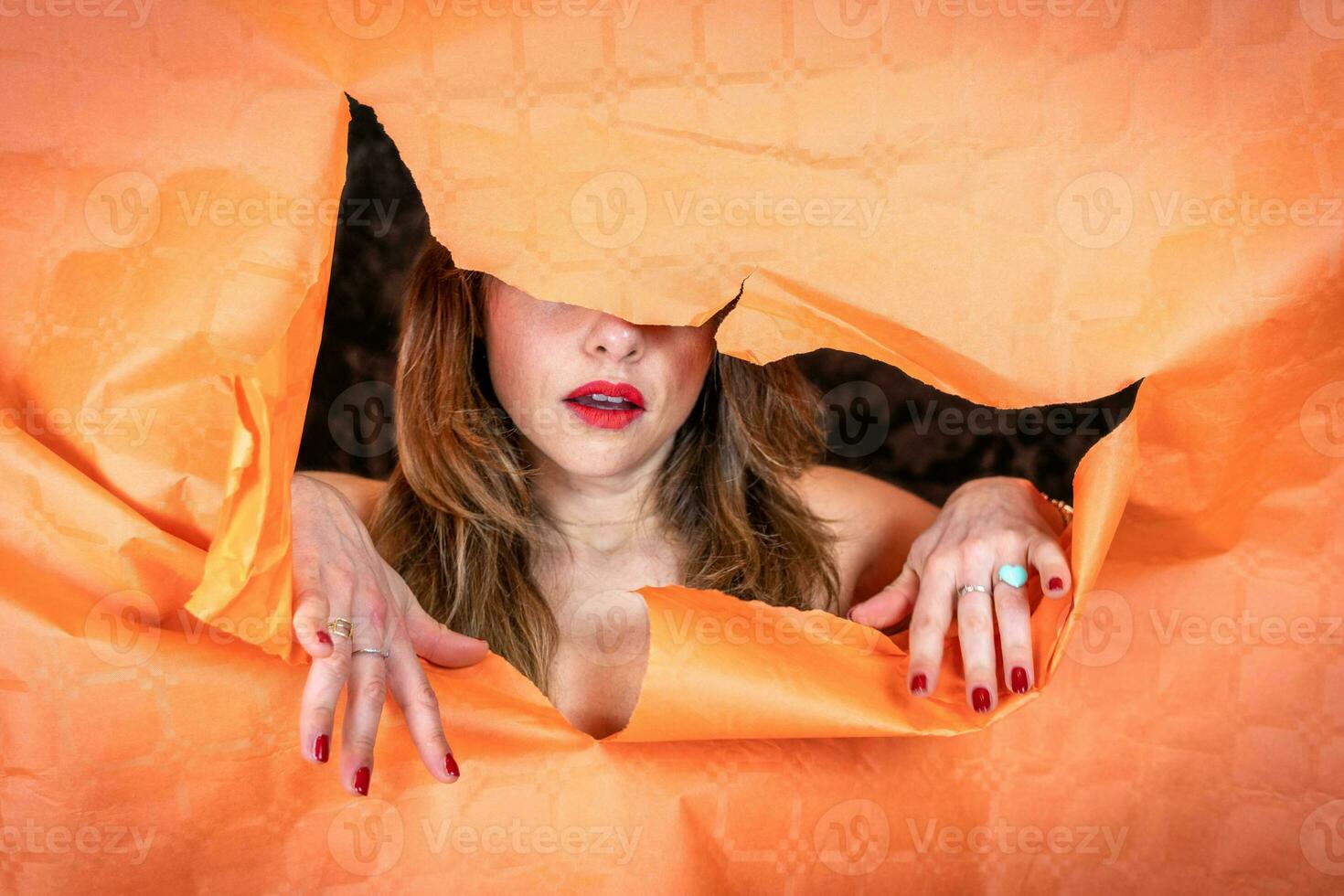 portrait of attractive young woman is coming out of a hole in a sheet of paper photo