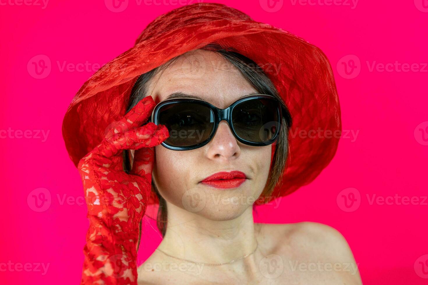 portrait of cute young woman wearing hat and red gloves on red background photo