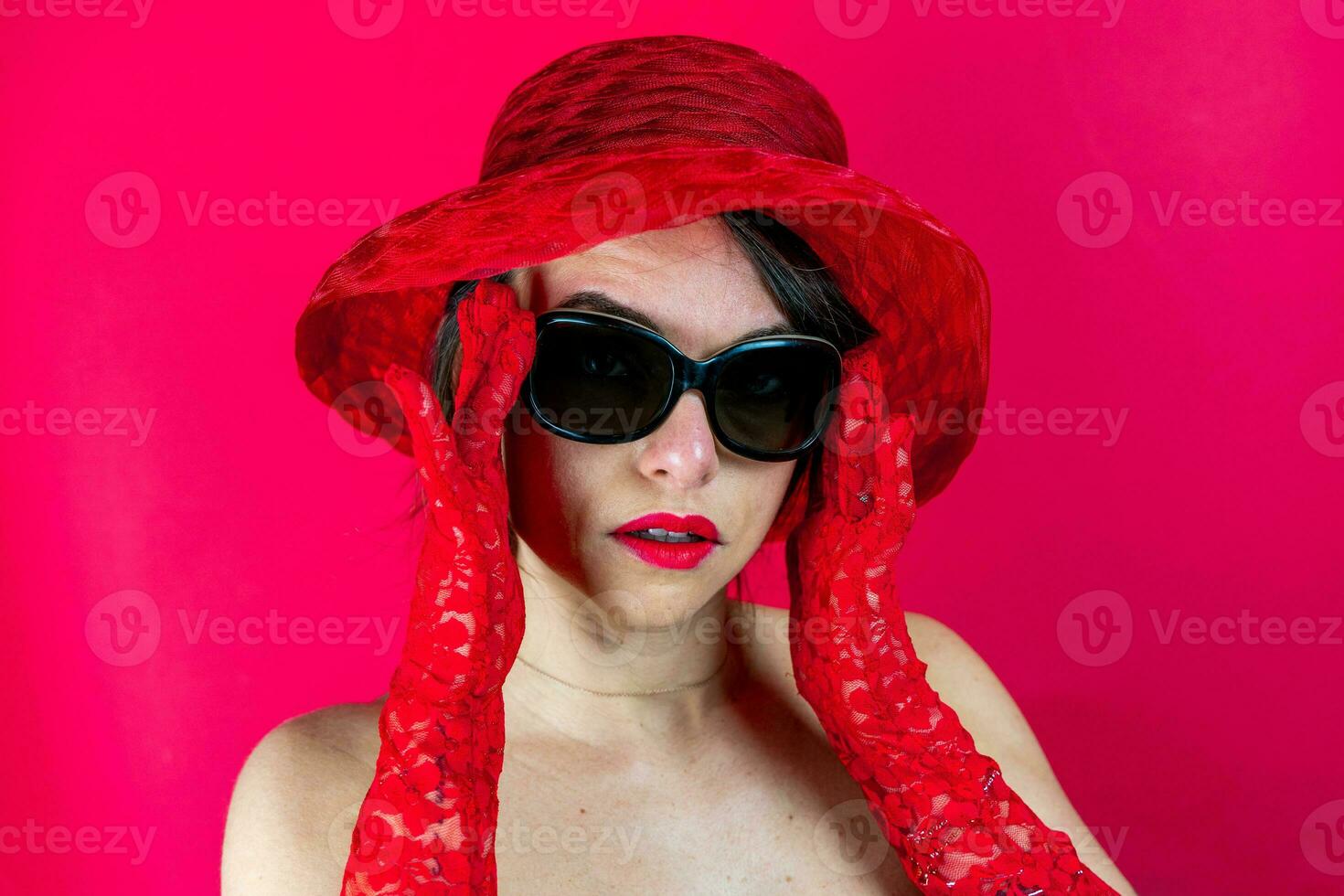 portrait of cute young woman wearing hat and red gloves on red background photo