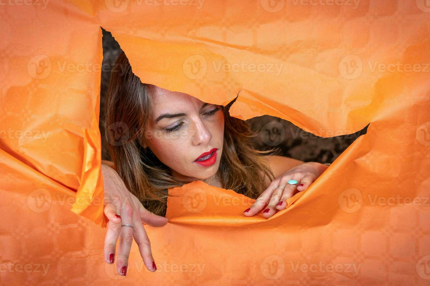 portrait of attractive young woman is coming out of a hole in a sheet of paper photo