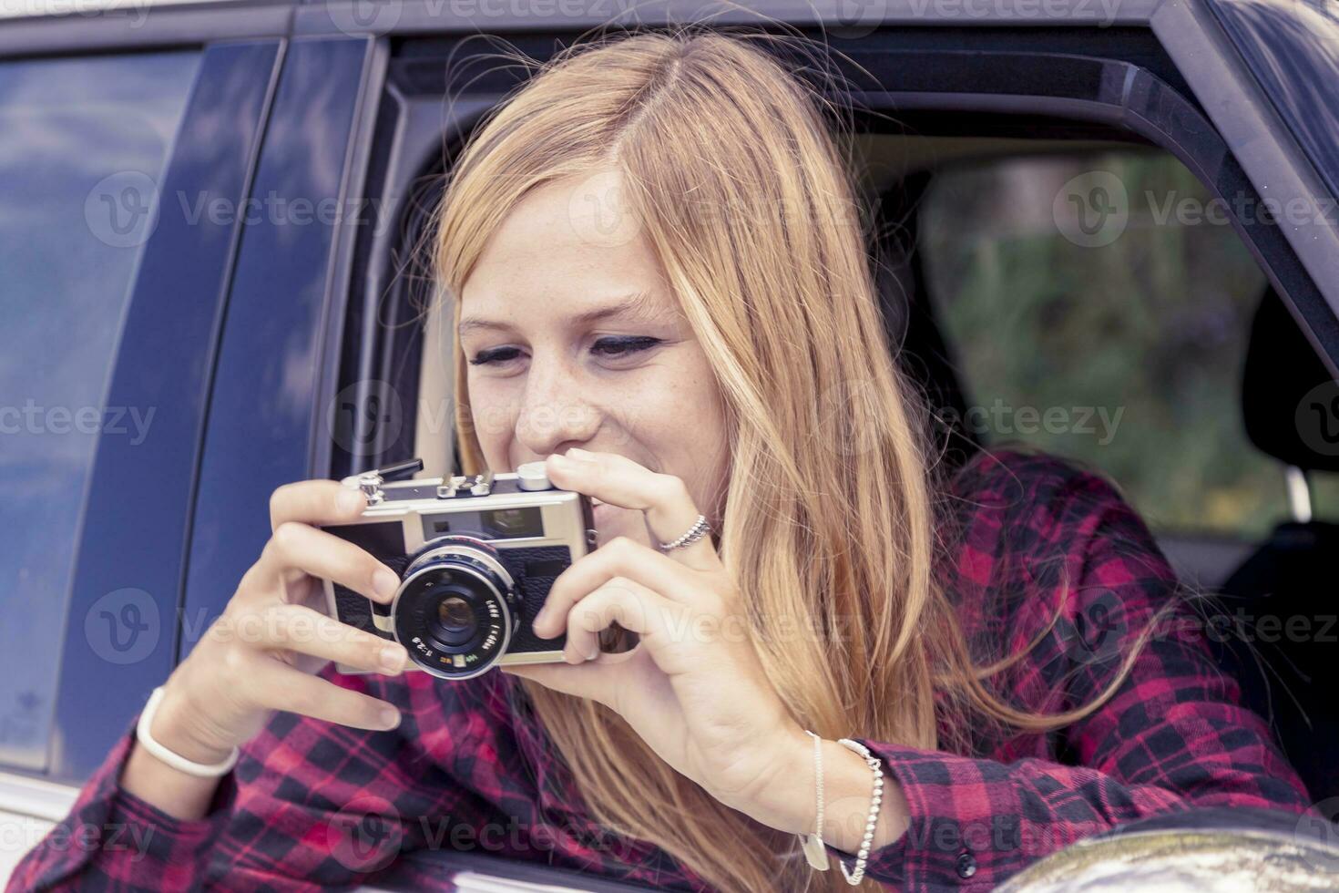 young blond girl takes a photo from a car