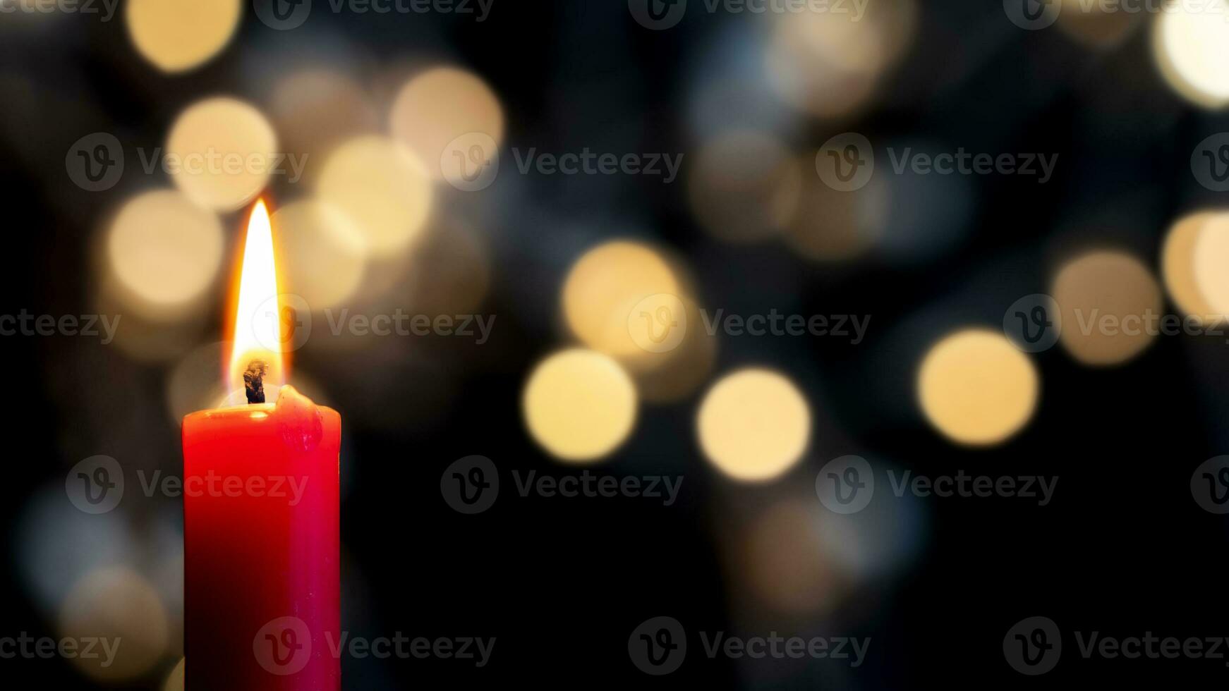 a red candle burns in the foreground in front of a colorful bokeh background photo