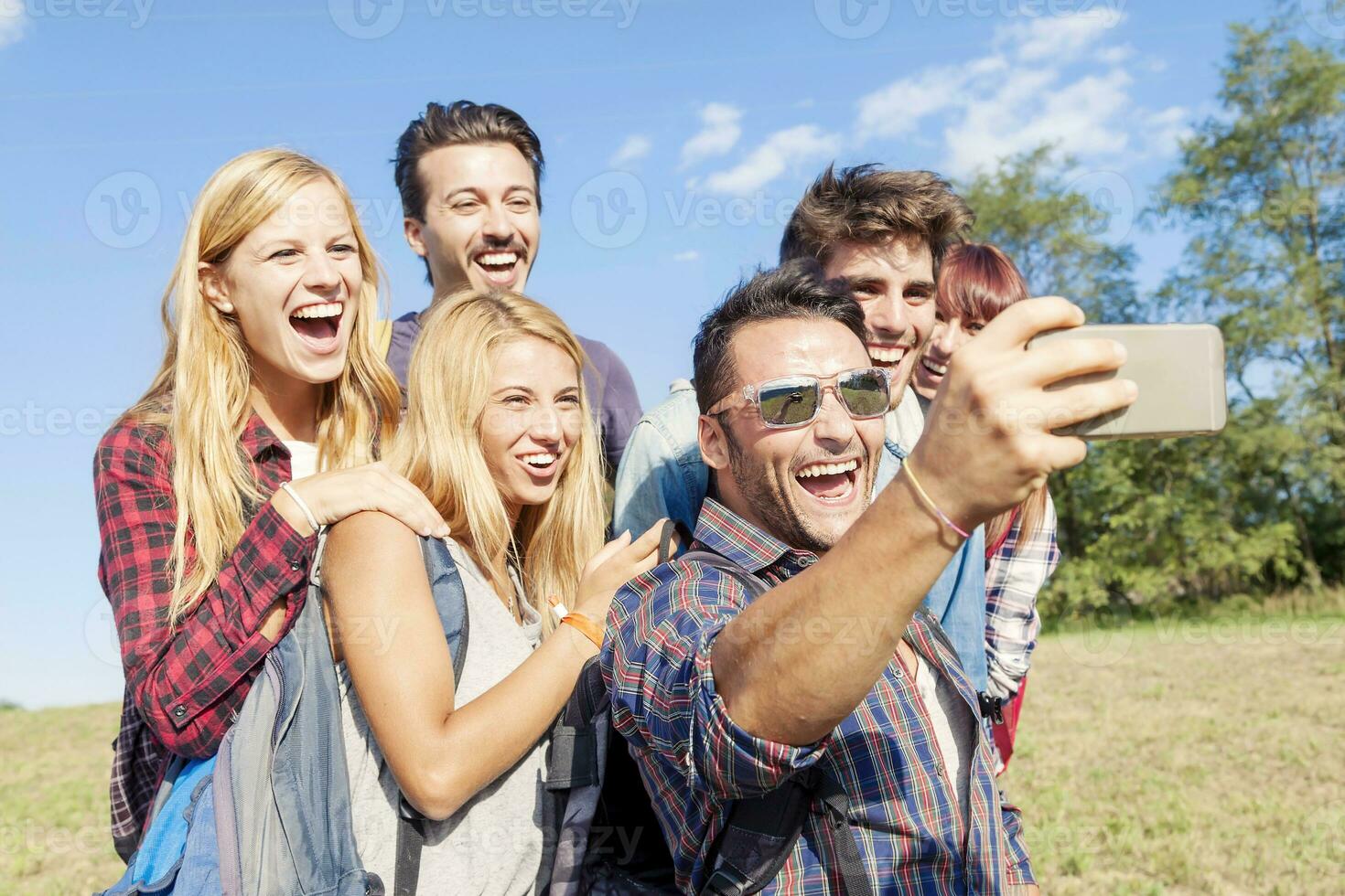 group of smiling friends taking selfie with smartphone photo