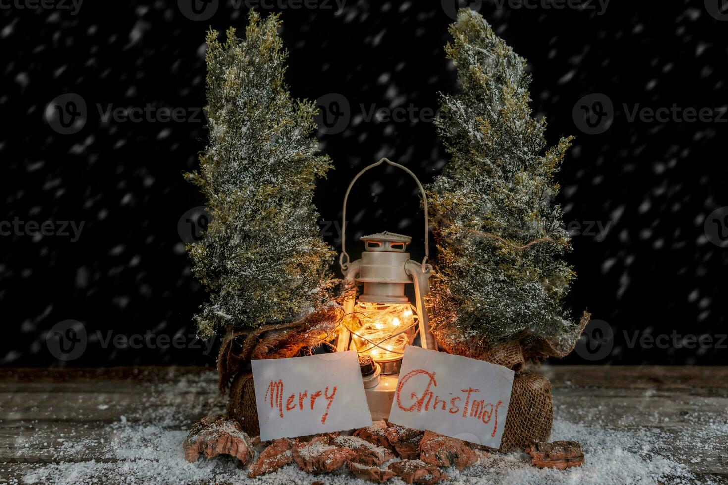 Christmas greeting cards hanging from two pine trees between a lantern in the snow photo