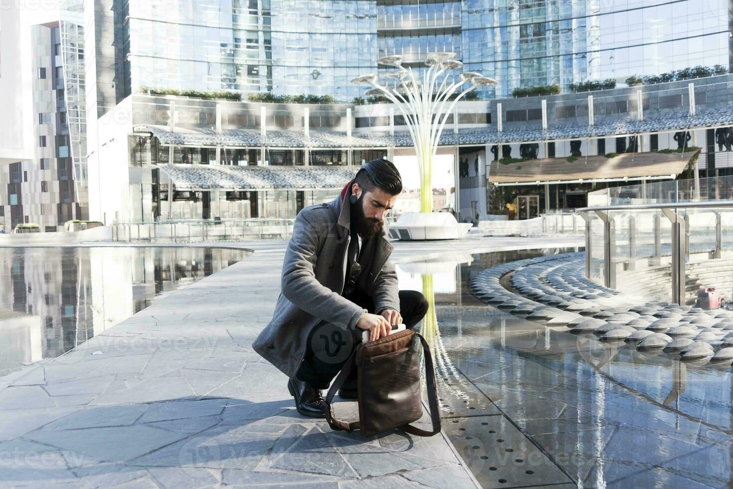 young hipster businessman consults his laptop in the heart of city photo