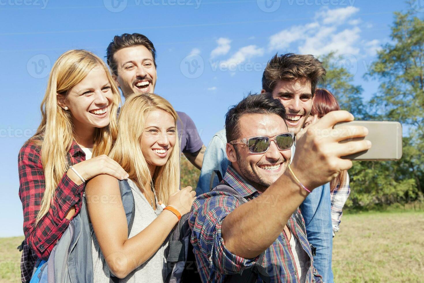 group of smiling friends taking selfie with smartphone photo