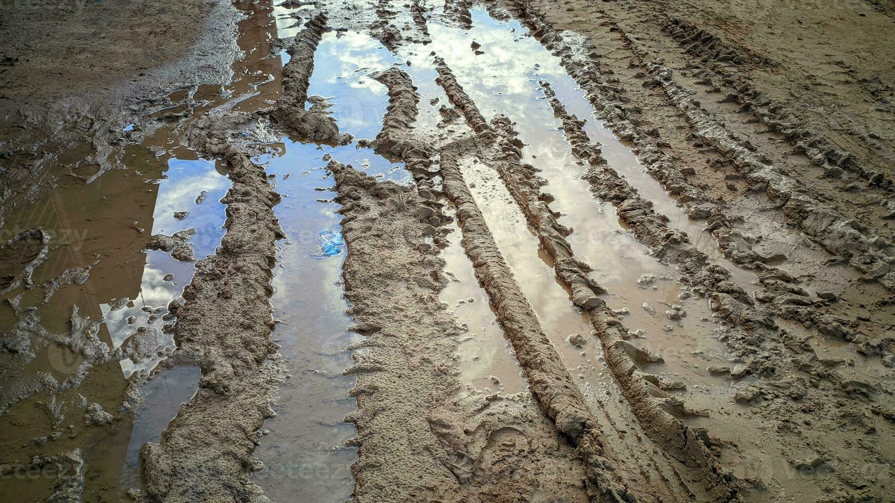 The road was muddy with tire marks and there were puddles of water photo