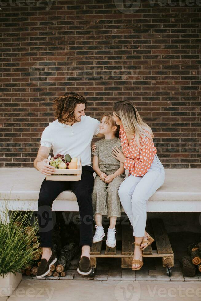 Family with a mother, father and daughter sitting outside on the steps of a front porch of a brick house photo