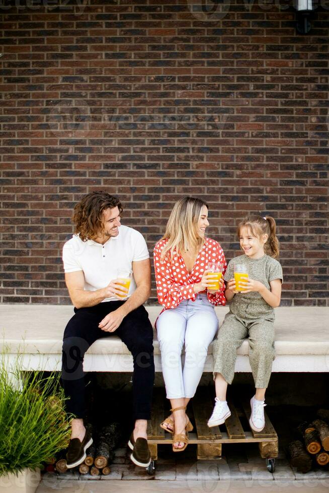 Family with a mother, father and daughter sitting outside on the steps of a front porch of a brick house photo