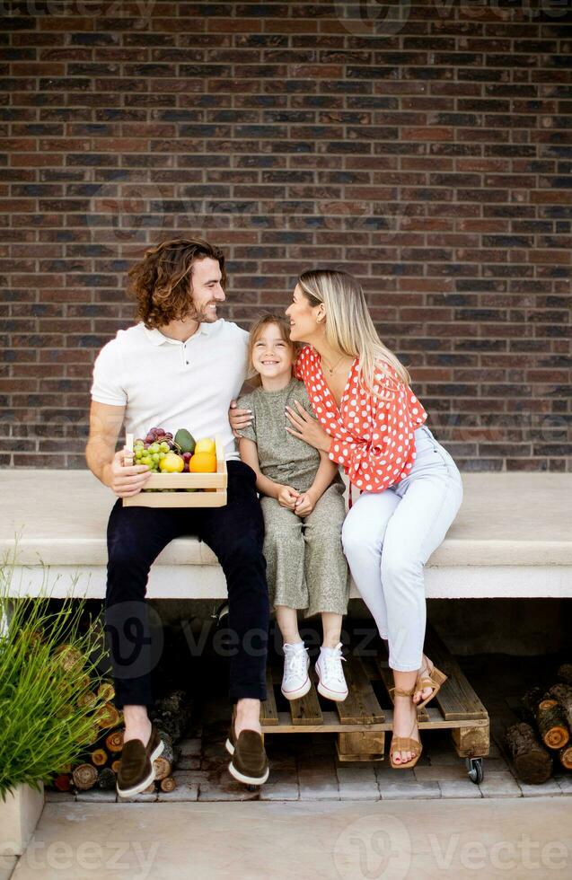 Family with a mother, father and daughter sitting outside on the steps of a front porch of a brick house photo