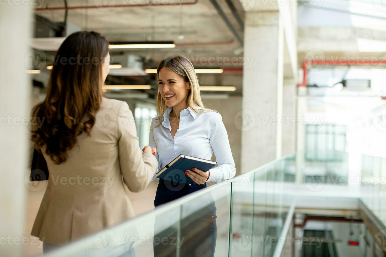 Two young business women with paper notebook in the office hallway photo