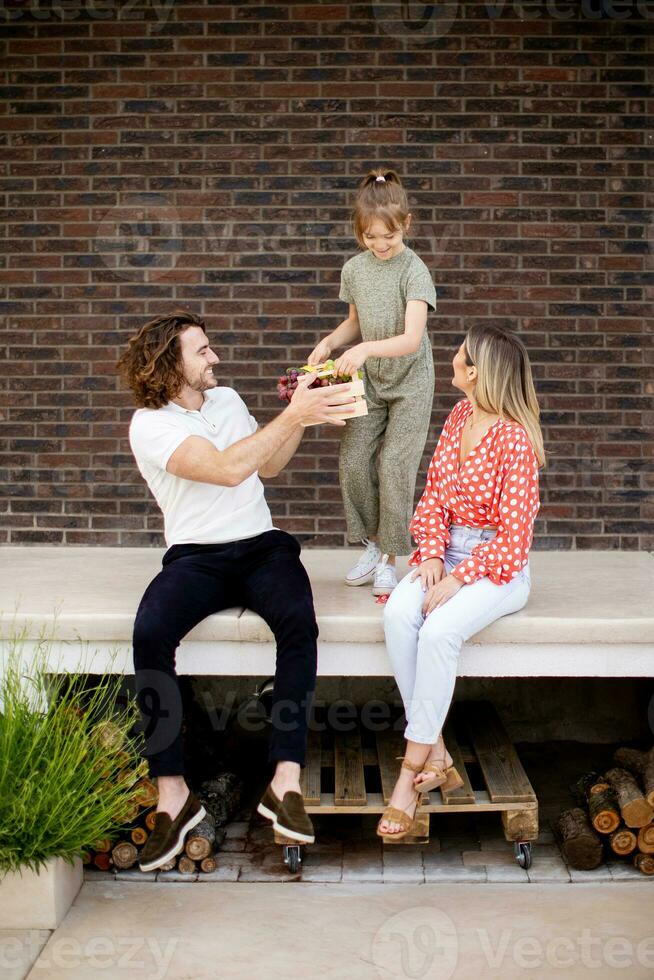 Family with a mother, father and daughter sitting outside on the steps of a front porch of a brick house photo