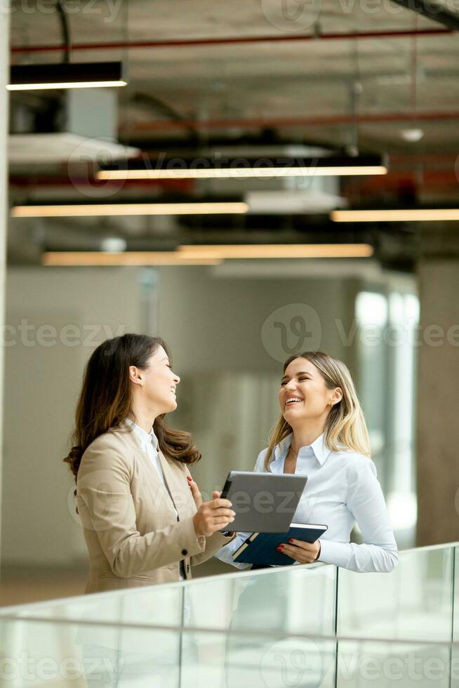 Two young business women with digital tablet in the office hallway photo