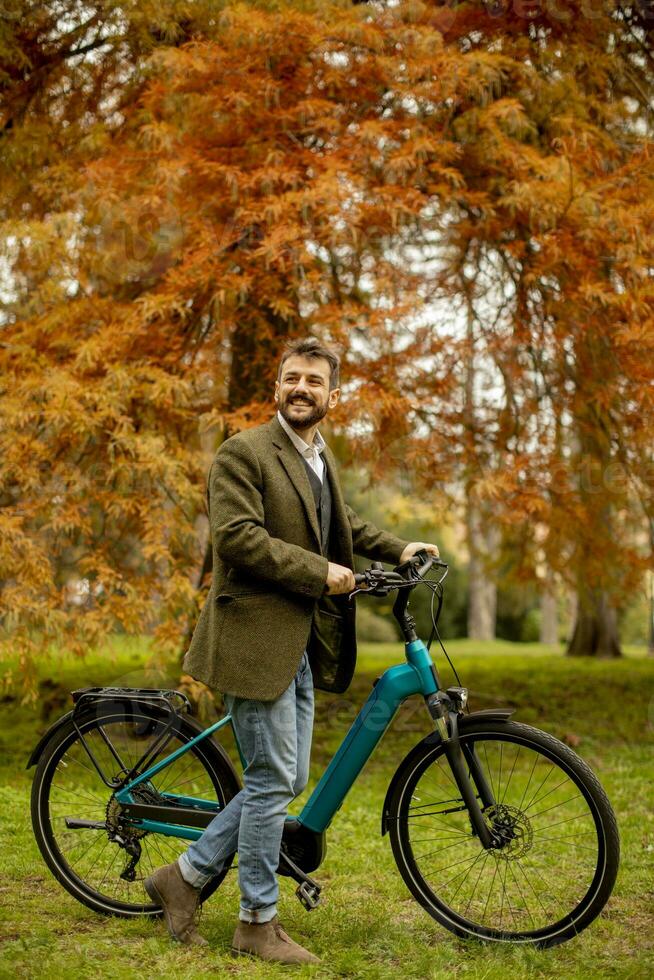 Handsome young man with electric bicycle in the autumn park photo