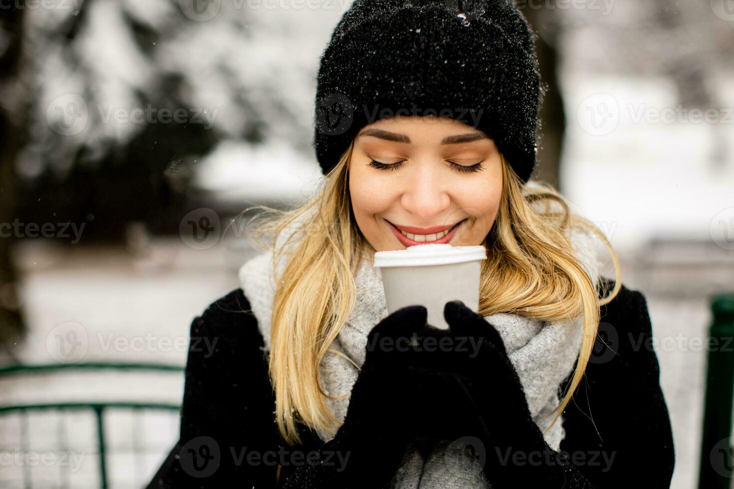 Young woman n warm clothes enjoying in snow with takeaway coffee cup photo