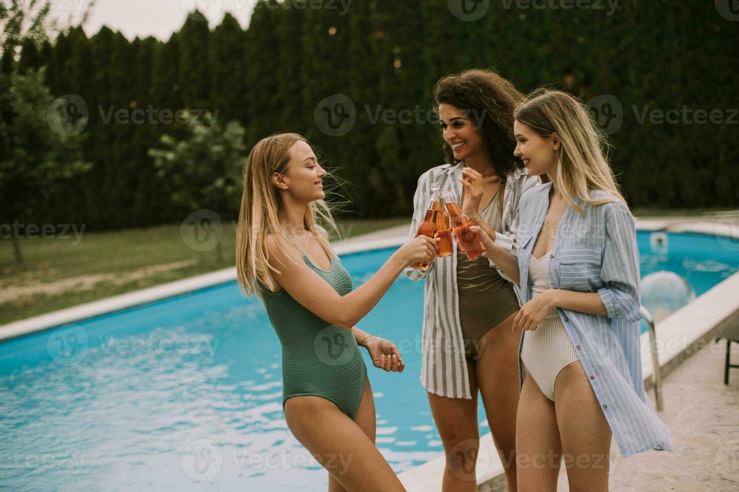 Three women enjoy a relaxing day by the swimming pool, sipping on refreshing cider photo