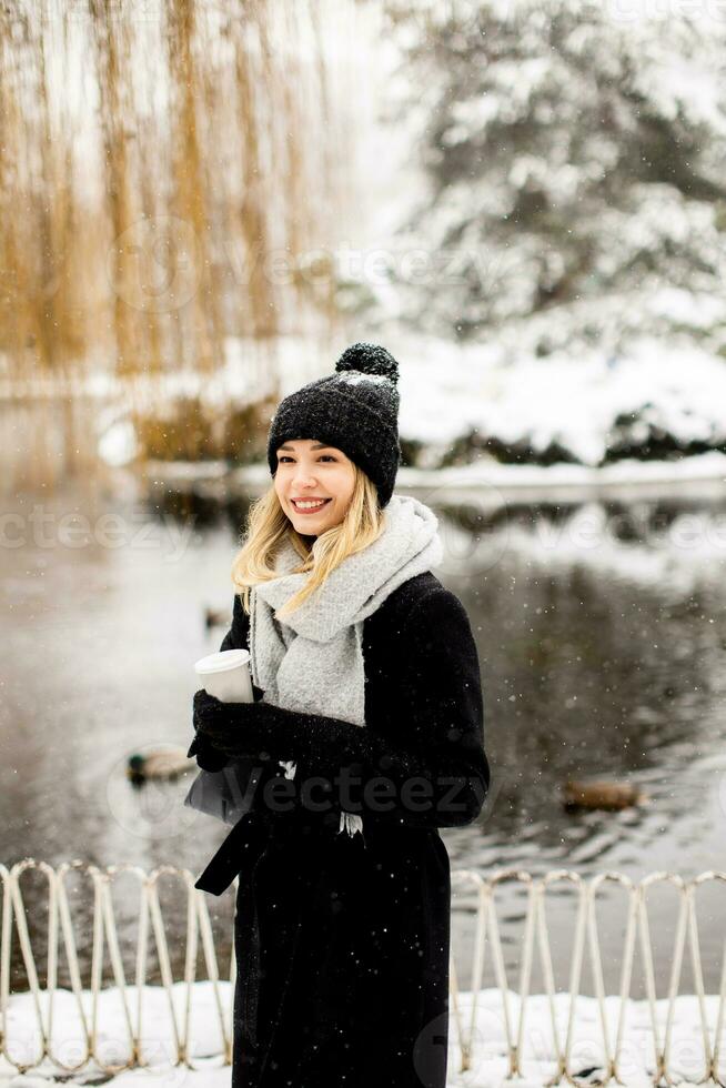 Young woman in warm clothes enjoying in snow with takeaway coffee cup photo